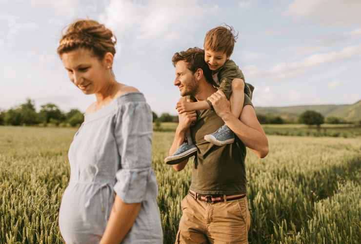 Familie im Kornfeld: Vater trägt Kind auf den Schultern. Mutter im Vordergrund.