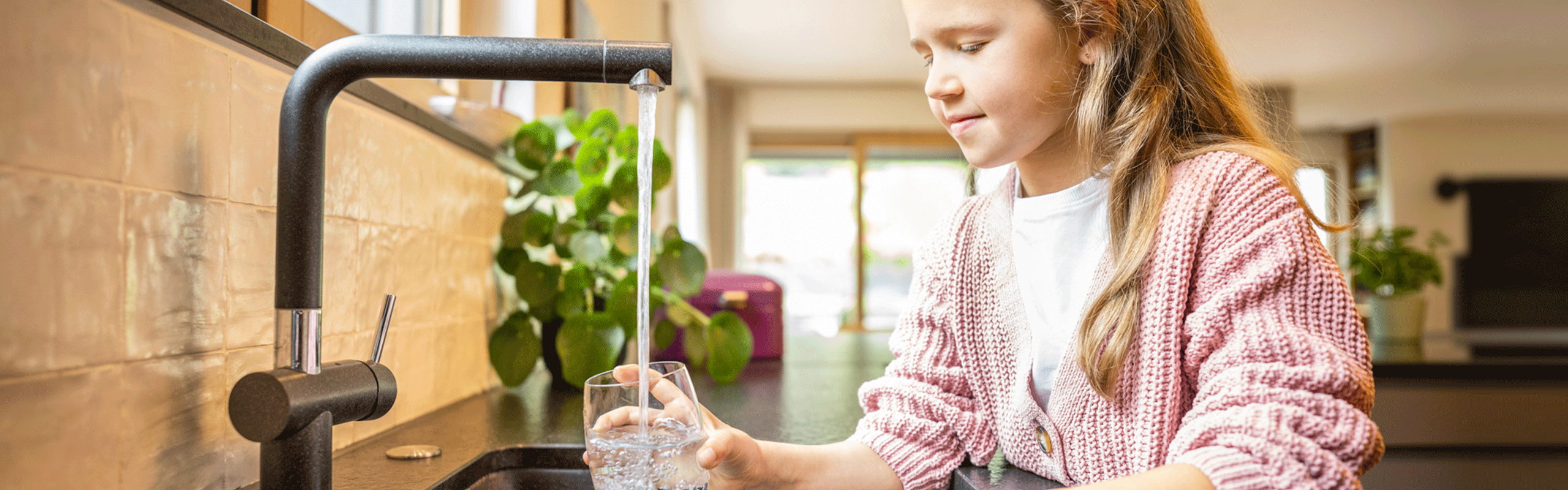 Mädchen füllt Wasserglas in Küche auf