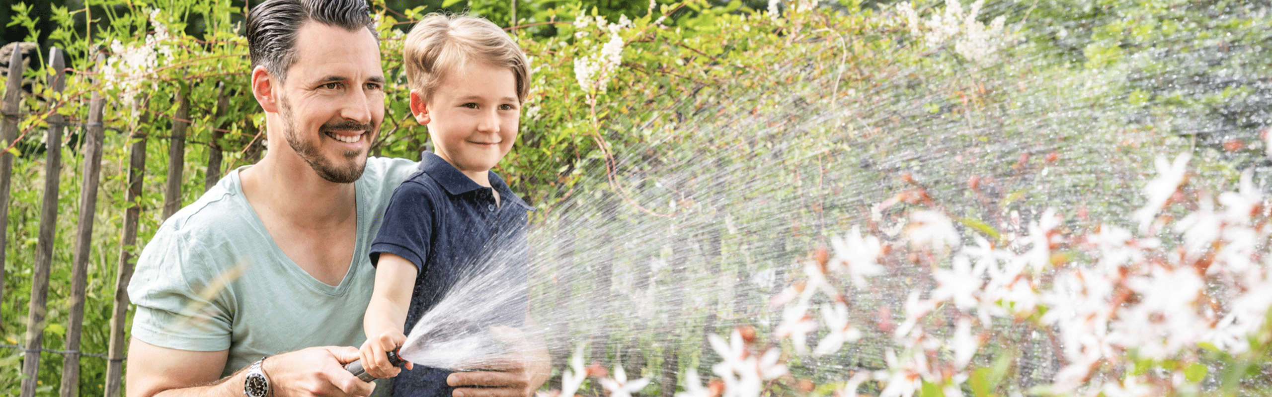 Vater und Sohn wässern den Garten mit Wasserschlauch